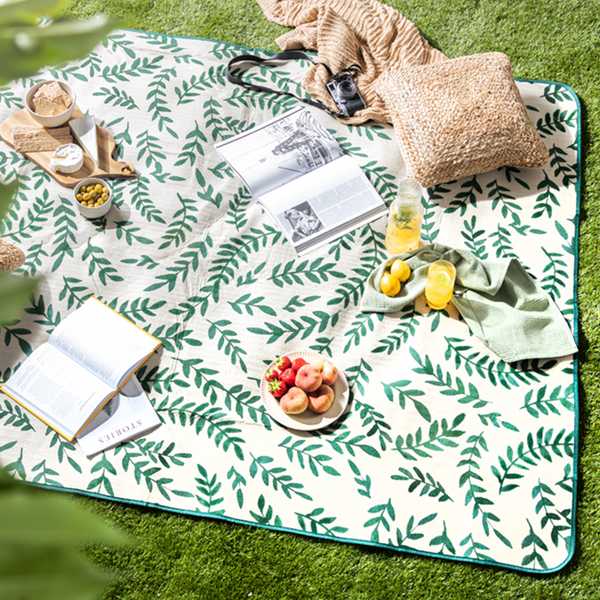 An outdoor pic nic set up with a leaf print blanket and wicker cushions.